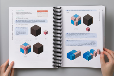 Designer holding the teacher book open to show a page of isometric illustrations of Montessori trinomial math learning cubes.