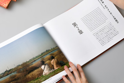 The designer showing the double-page opener for chapter 2, with a large full-page image of friends sitting on the banks of a river in Matsudo, Japan.